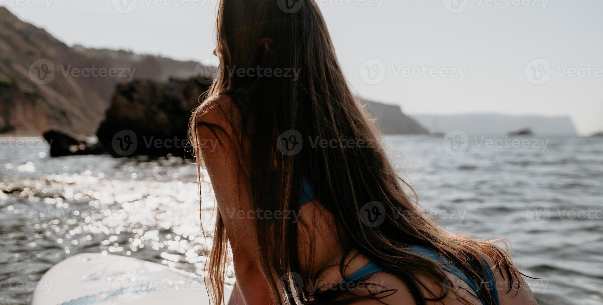 mulher mar e aí. fechar acima retrato do feliz jovem caucasiano mulher com grandes cabelo olhando às Câmera e sorridente. fofa mulher retrato dentro uma azul bikini posando em sup borda dentro a mar foto