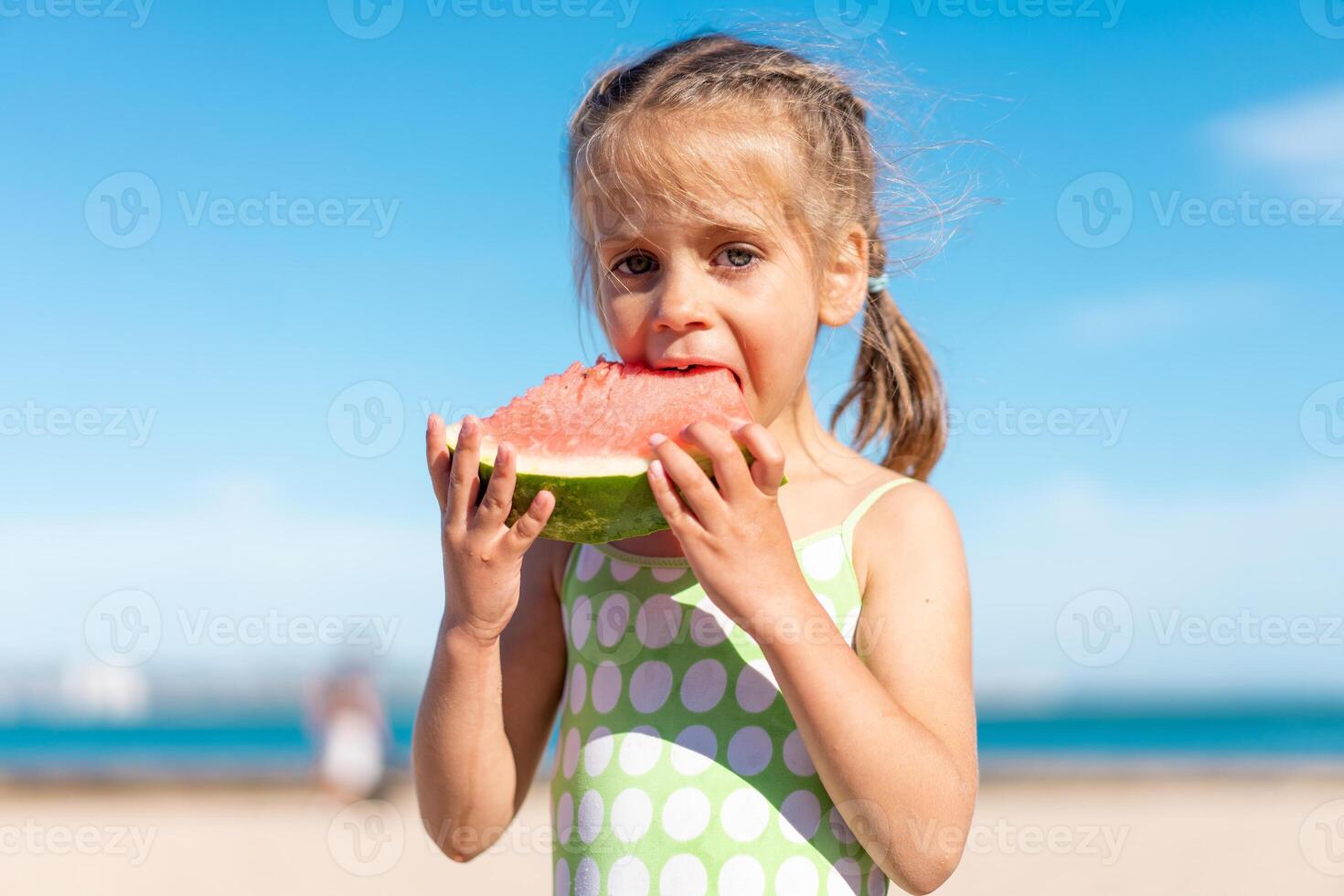 engraçado pequeno menina comer Melancia ensolarado verão dia às oceano de praia. fofa caucasiano fêmea criança apreciar verão fruta mordida fatia do Melancia. feliz infância. foto