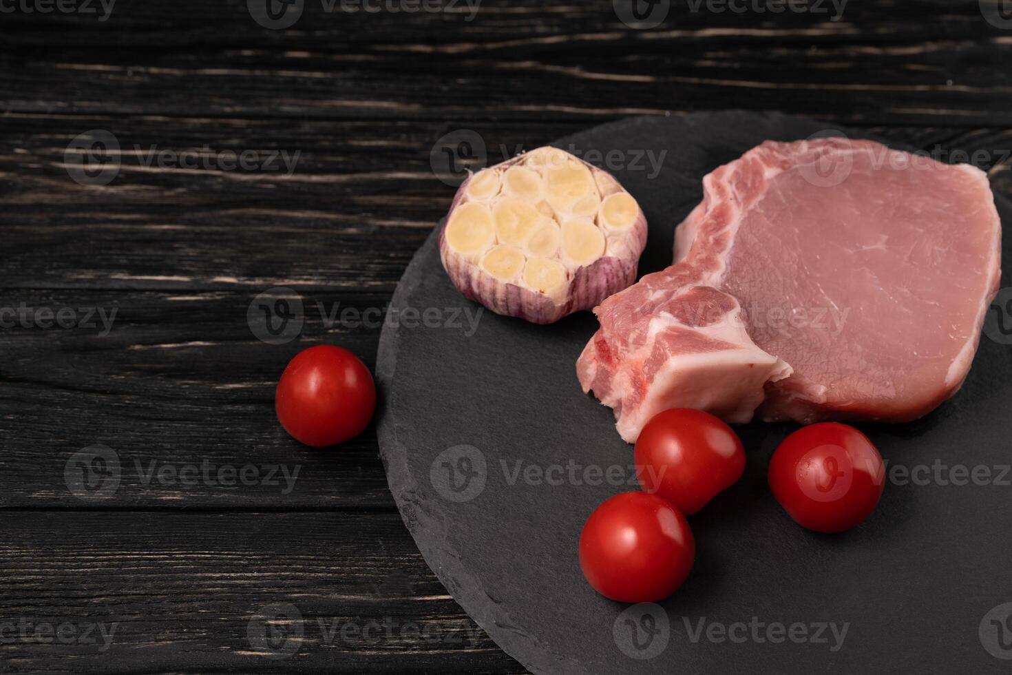 topo Visão do 1 peças cru carne de porco Picar bifes com cereja tomates e alho em uma Preto pedra corte borda. foto