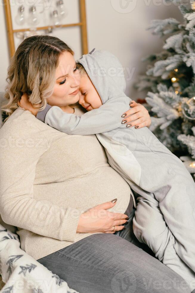 mãe tocam com criança. feliz família retrato dentro casa grávida mãe abraços dele pequeno filho. foto