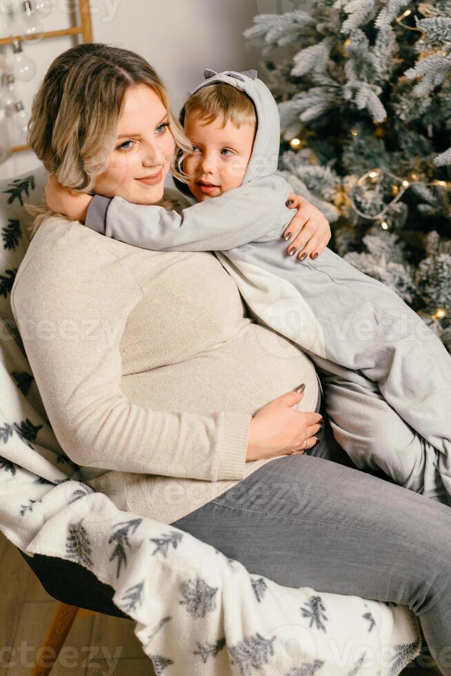 mãe tocam com criança. feliz família retrato dentro casa grávida mãe abraços dele pequeno filho. foto