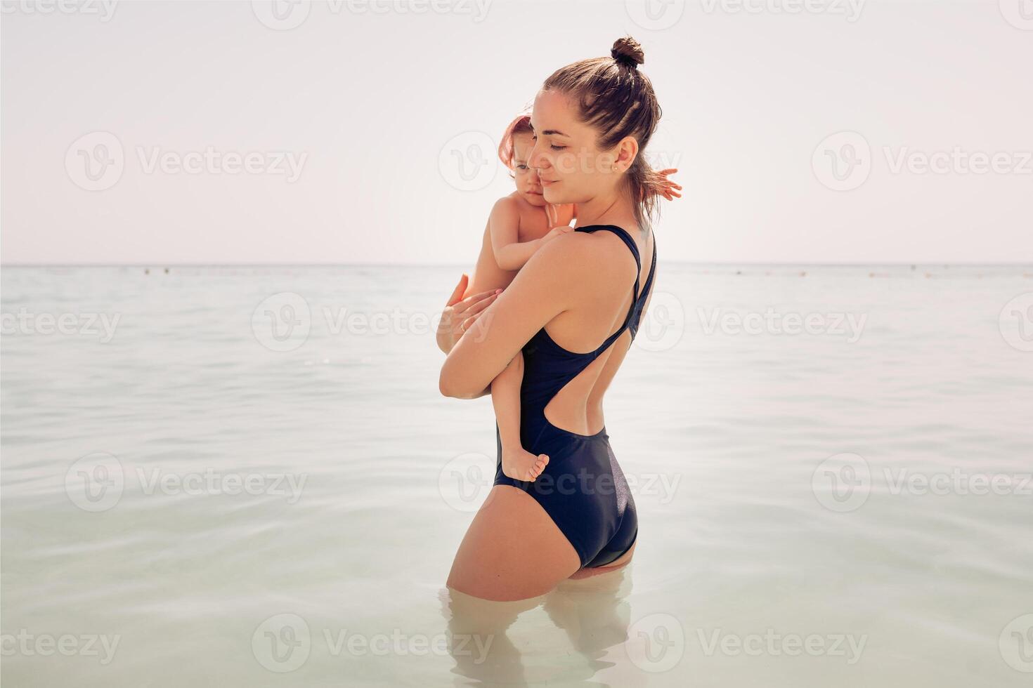 mãe com uma pequeno filha estão até a cintura dentro a mar água foto