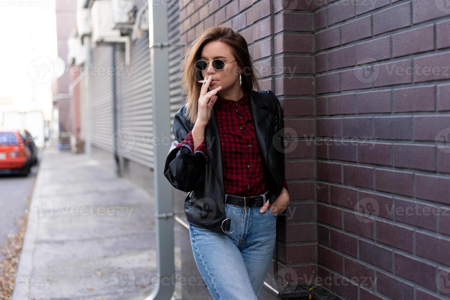 lindo jovem elegantemente vestido caucasiano menina fuma cigarro em a rua. foto