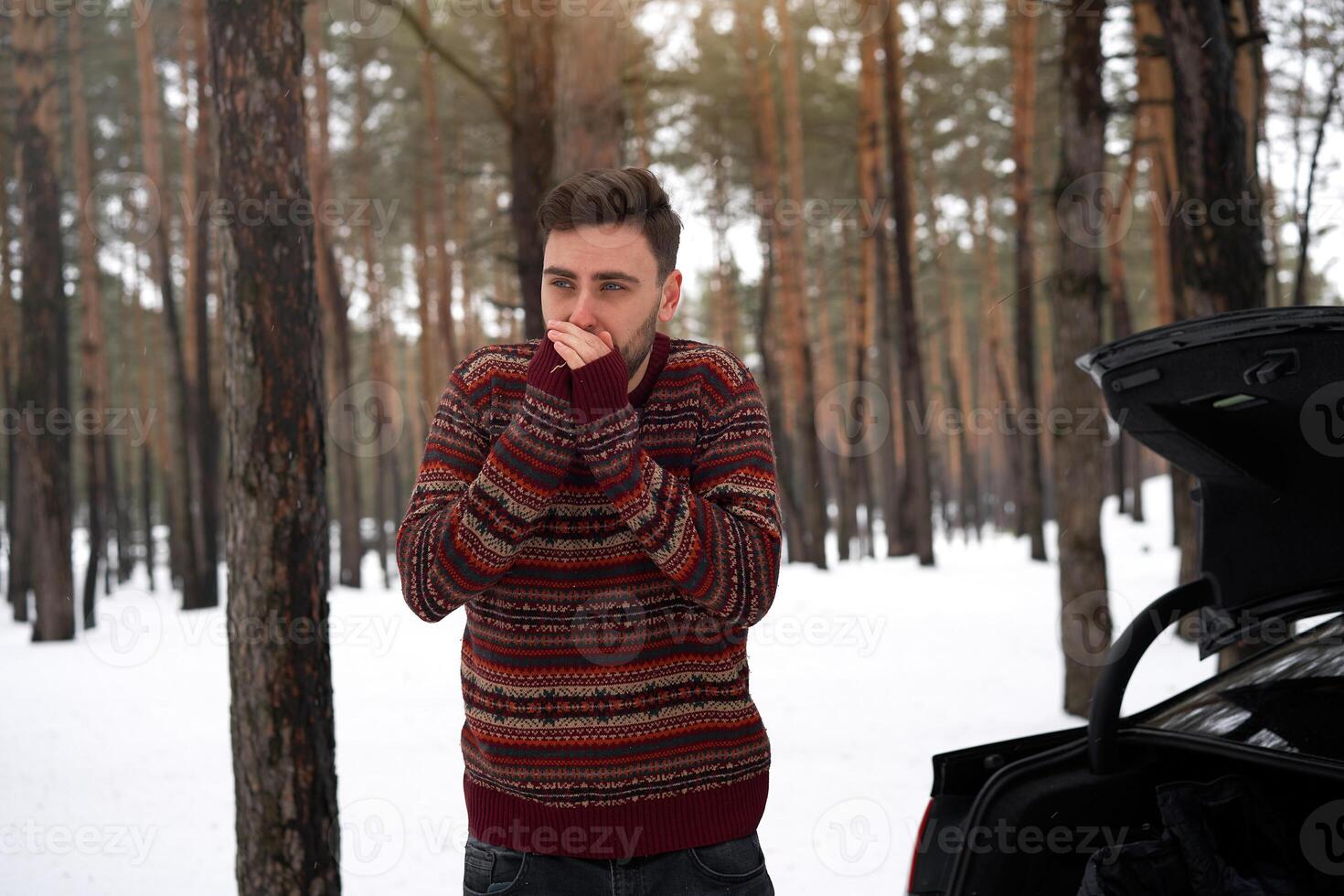 jovem adulto bonito homem em pé dentro inverno floresta perto dele carro. atraente caucasiano cara esperando para Socorro quando carro é quebrado. foto