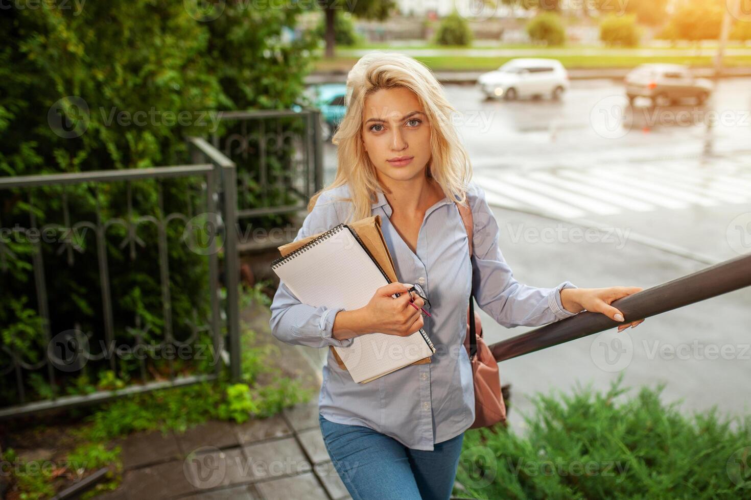 entusiasmado sério lindo jovem menina segurando pilha do livros em pé perto campus estilo de vida positividade acadêmico graduando universidade escola foto