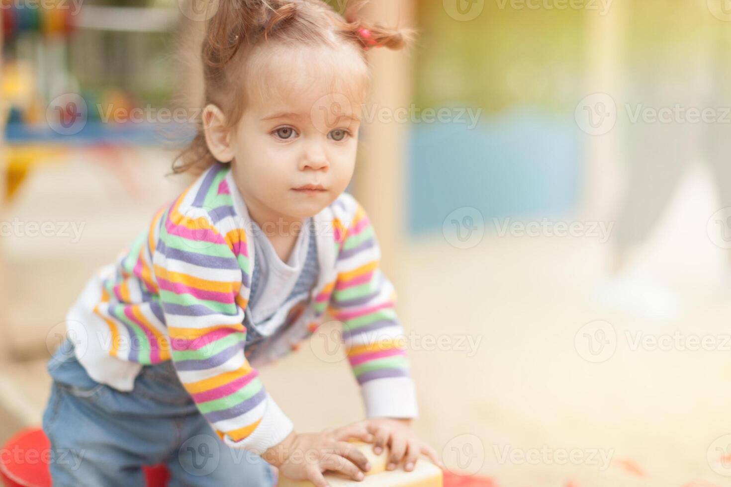 uma pequeno menina com dois caudas dentro uma listrado blusa tocam uma verão ensolarado dia dentro a Parque infantil foto