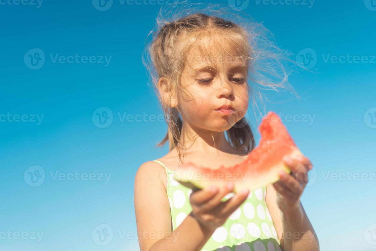 engraçado pequeno menina comer Melancia ensolarado verão dia às oceano de praia. fofa caucasiano fêmea criança apreciar verão fruta mordida fatia do Melancia. feliz infância. foto