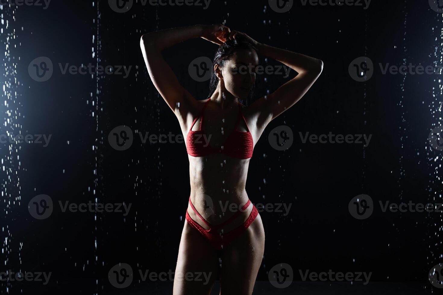 lindo jovem menina dentro vermelho roupa de esporte poses dentro aqua estúdio. gotas do água espalhar sobre dela ginástica corpo. a perfeito figura em a fundo do água salpicos foto