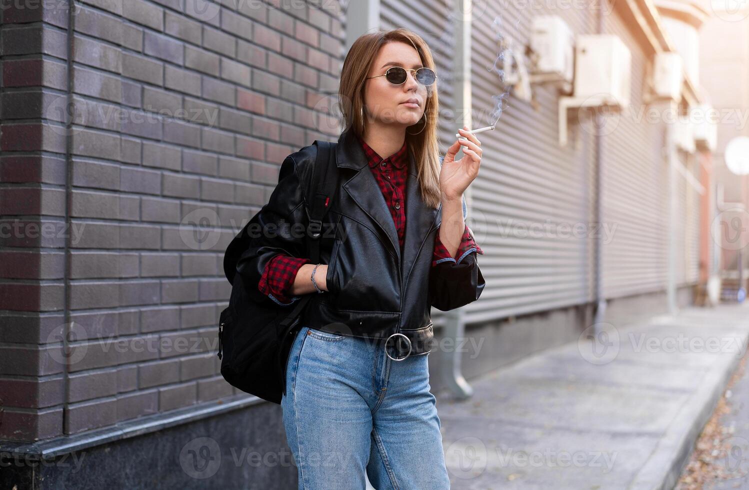 lindo jovem elegantemente vestido caucasiano menina fuma cigarro em a rua. foto