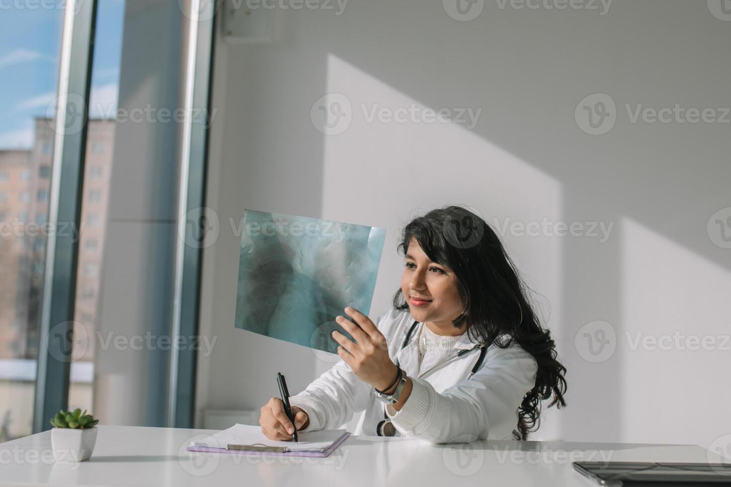 jovem indiano médico aluna às a clínica dentro prática. fêmea médico dentro branco casaco com estetoscópio examina raio X foto