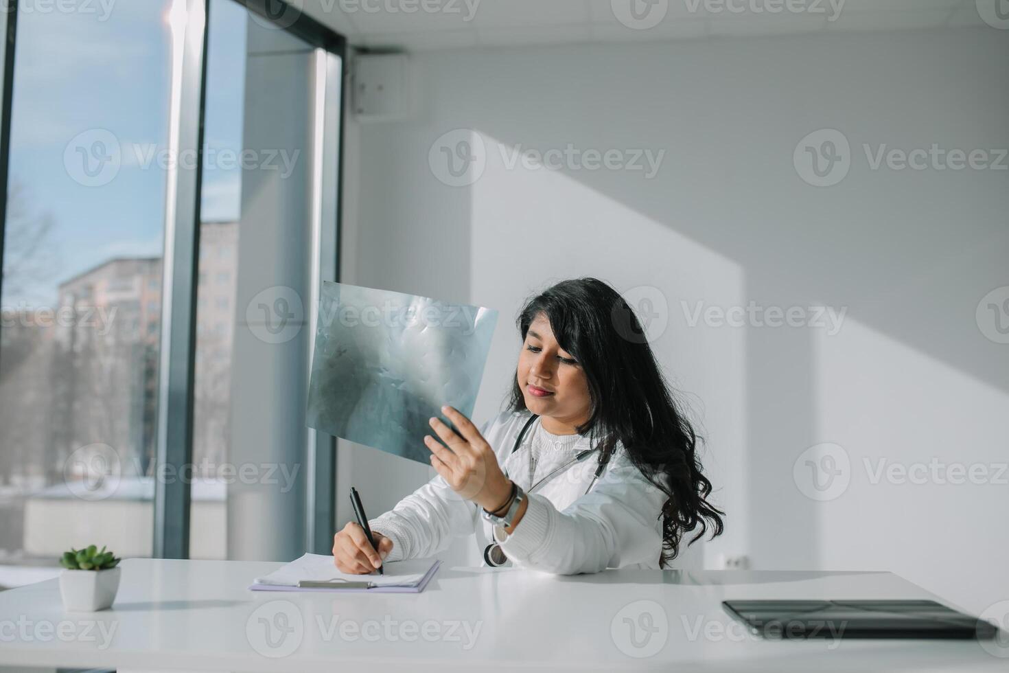 jovem indiano médico aluna às a clínica dentro prática. fêmea médico dentro branco casaco com estetoscópio examina raio X foto