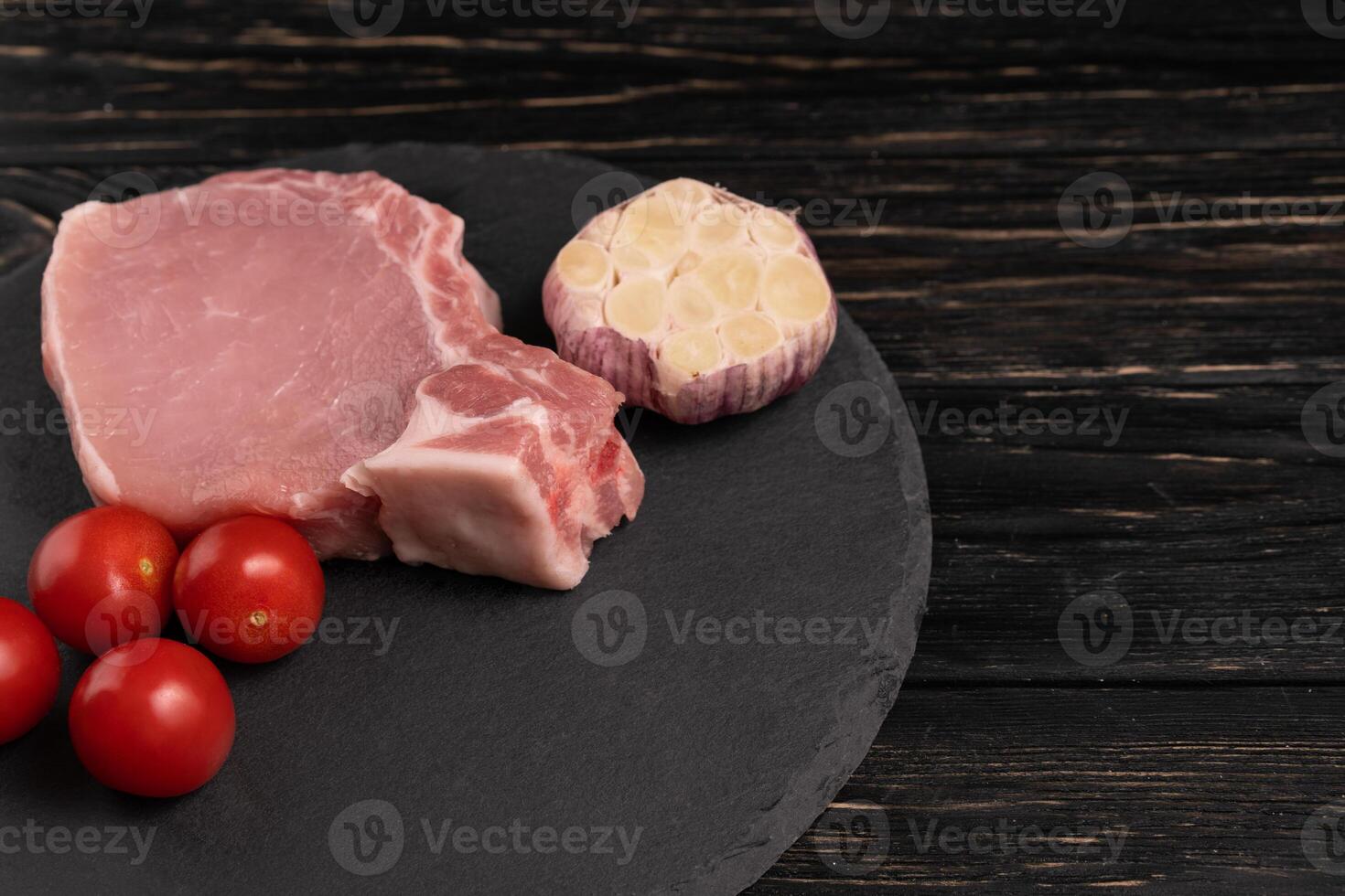 topo Visão do 1 peças cru carne de porco Picar bifes com cereja tomates e alho em uma Preto pedra corte borda. foto