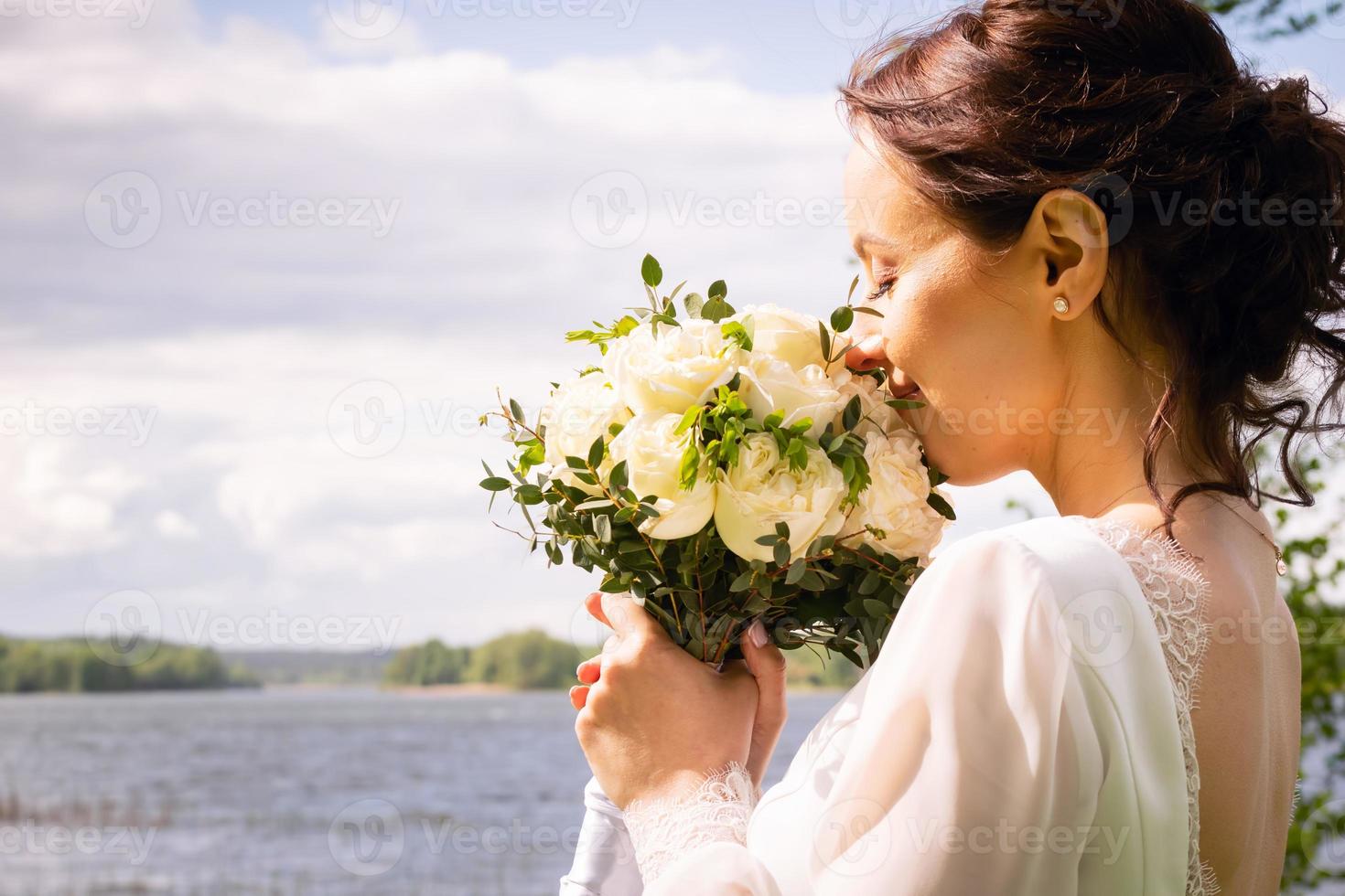 bela jovem caucasiana cheirar buquê de rosa branca na natureza com fundo ensolarado. conceito de casamento feliz foto