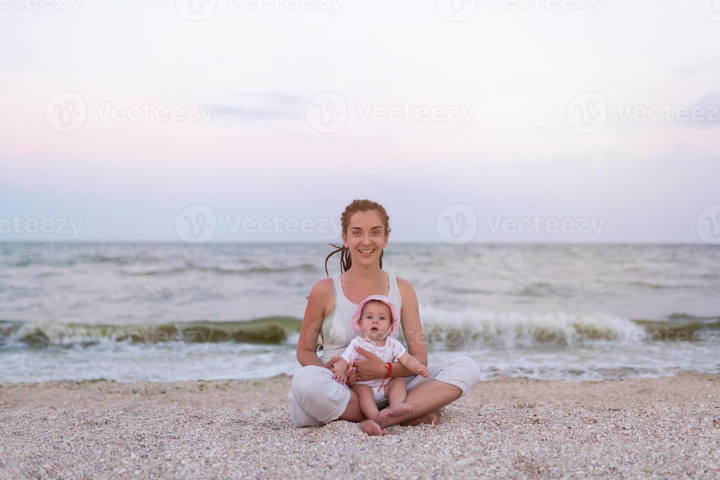 feliz família mãe e criança filha fazendo ioga, meditar dentro lótus posição em de praia às pôr do sol foto