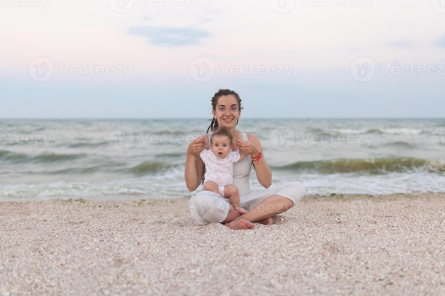 feliz família mãe e criança filha fazendo ioga, meditar dentro lótus posição em de praia às pôr do sol foto
