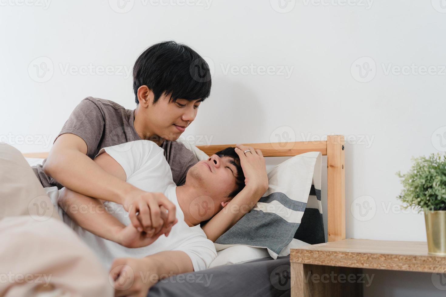 casal gay asiático beija e abraça na cama em casa. jovens asiáticos lgbtq homens felizes relaxam descansam juntos, passam um tempo romântico depois de acordar no quarto em casa no conceito de manhã. foto