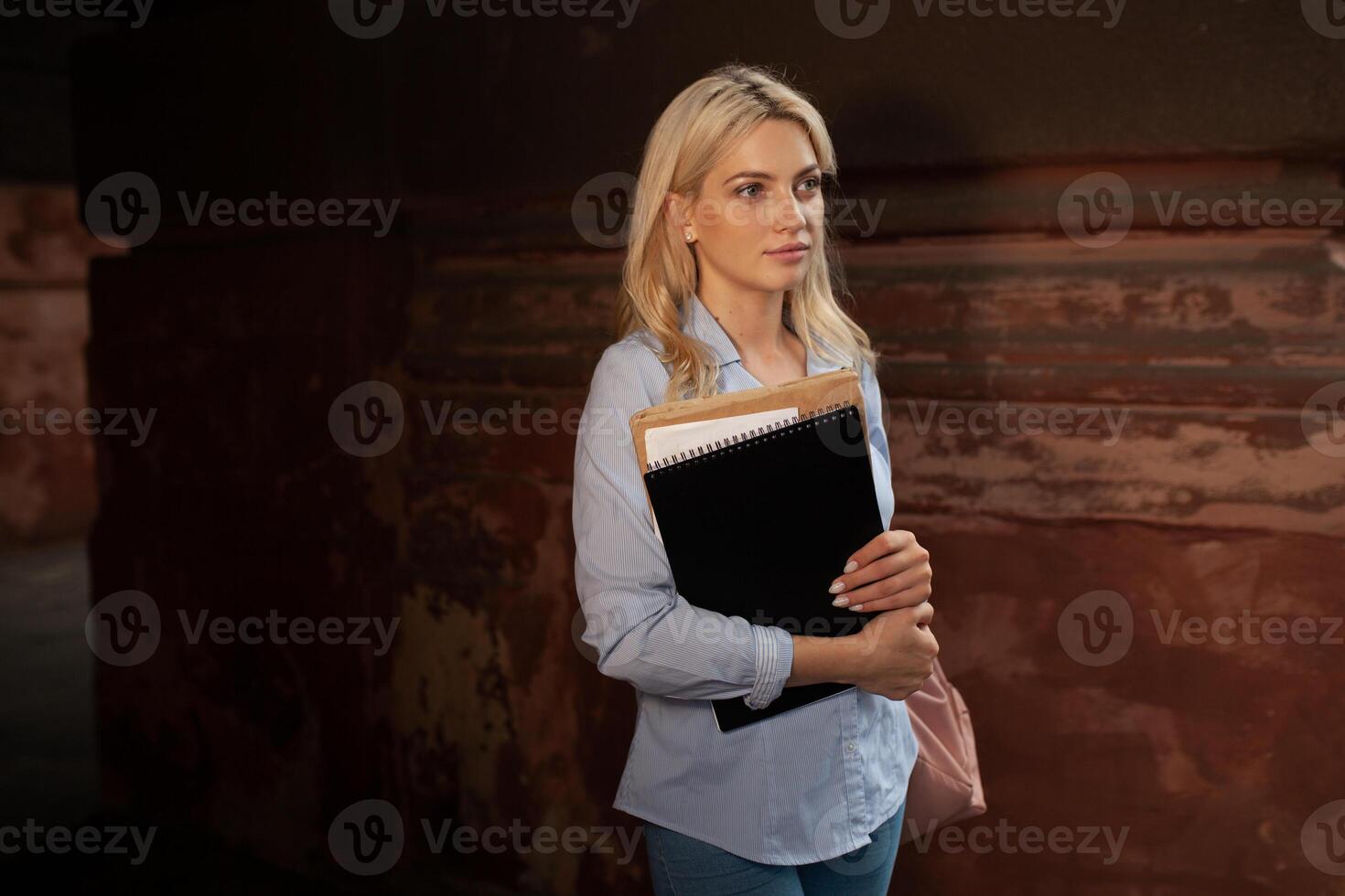 entusiasmado sério lindo jovem menina segurando pilha do livros em pé perto campus estilo de vida positividade acadêmico graduando universidade escola foto