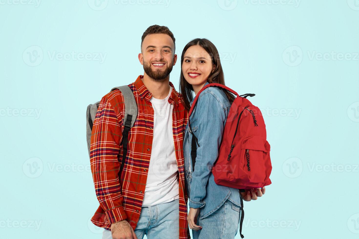 jovem casal em pé com mochilas dentro estúdio sobre azul pano de fundo foto