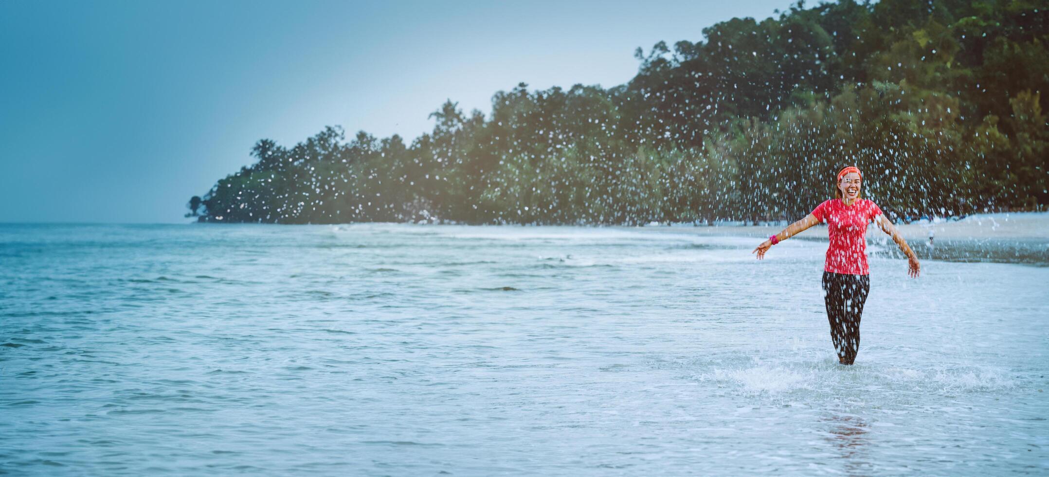 mulher asiática, treino de corrida na praia pela manhã. relaxe com a praia. divertido e feliz em brincar, pular, chutar o mar. no verão foto