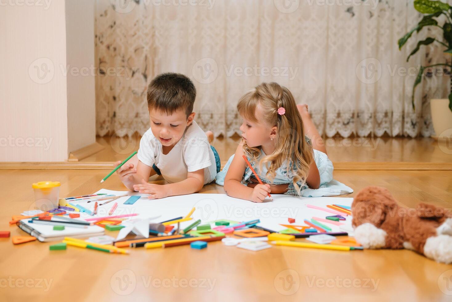 crianças desenhando em chão em papel. pré escola Garoto e menina jogar em chão com educacional brinquedos - blocos, trem, Ferrovia, avião. brinquedos para pré escola e Jardim da infância. crianças às casa ou creche foto