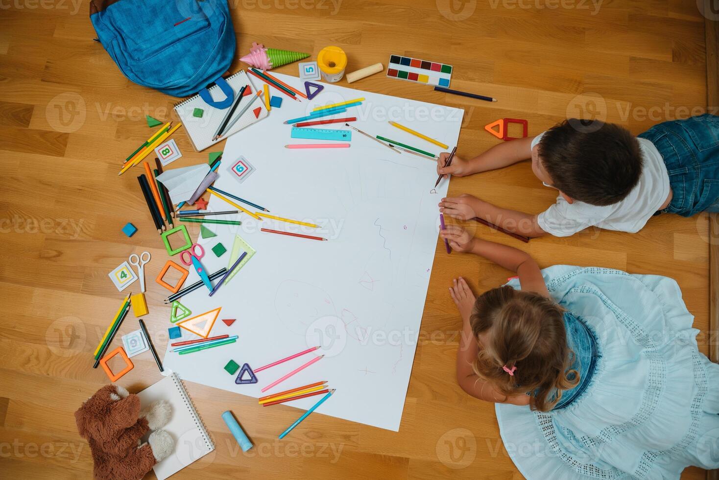 crianças desenhando em chão em papel. pré escola Garoto e menina jogar em chão com educacional brinquedos - blocos, trem, Ferrovia, avião. brinquedos para pré escola e Jardim da infância. crianças às casa ou creche. topo visualizar. foto