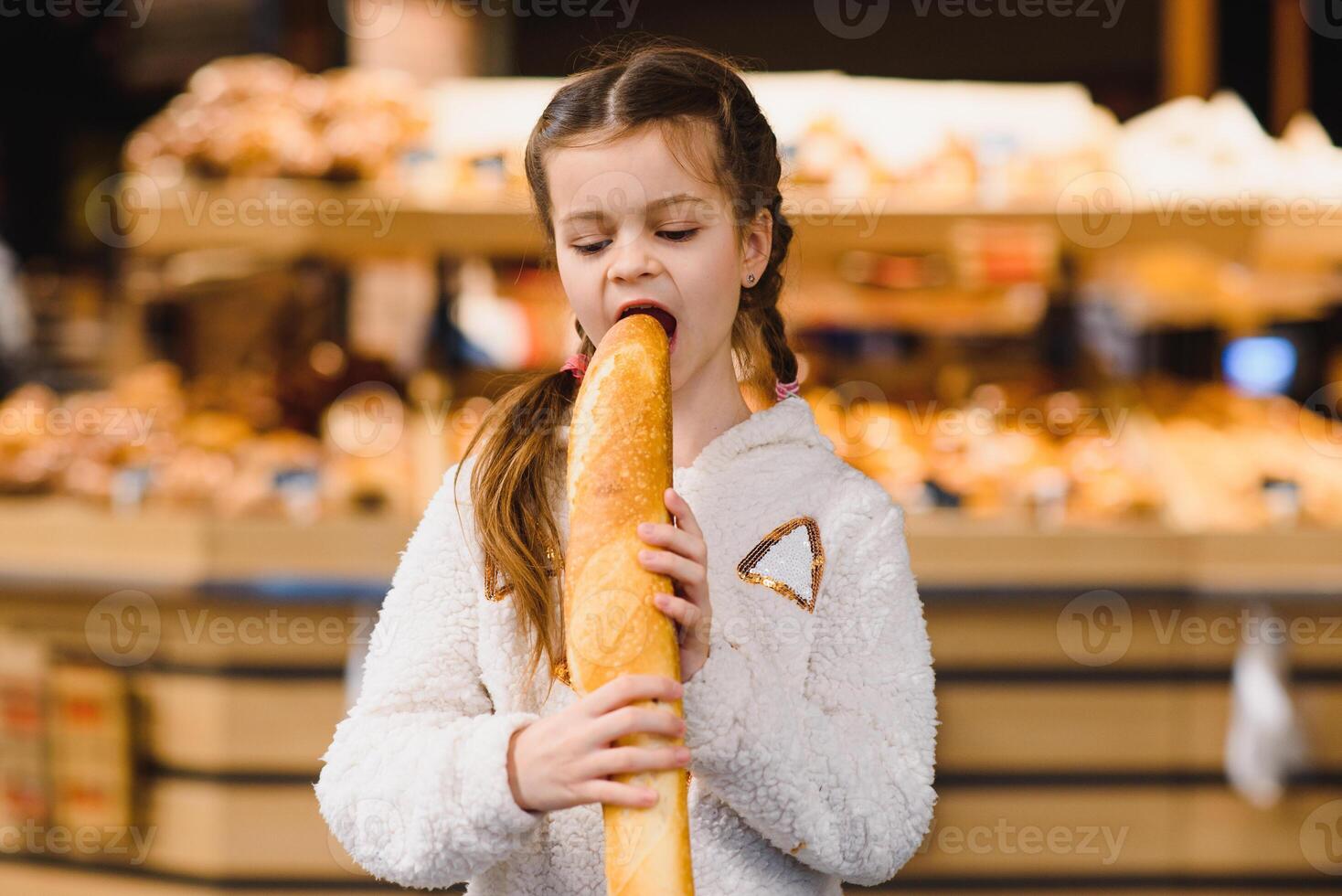 jovem e engraçado menina comendo baguetes dentro frente do a padaria loja foto