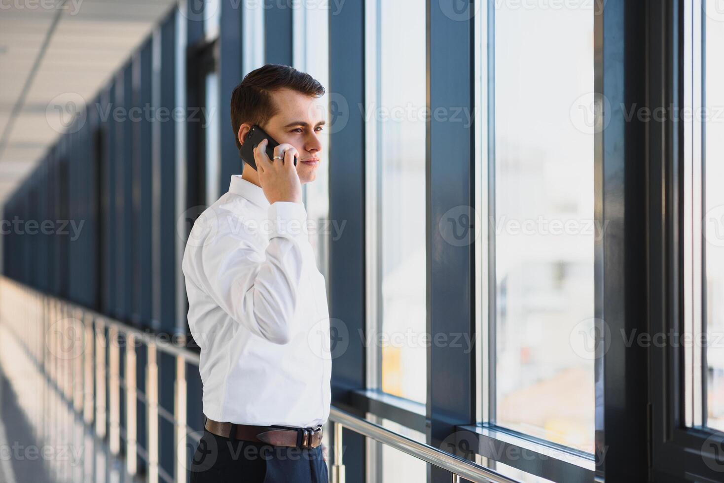 retrato do uma sério confiante homem patrão tendo Móvel telefone conversação enquanto em repouso depois de encontro com dele parceiros, homem de negocios falando em célula Telefone enquanto em pé dentro moderno espaço dentro de casa foto