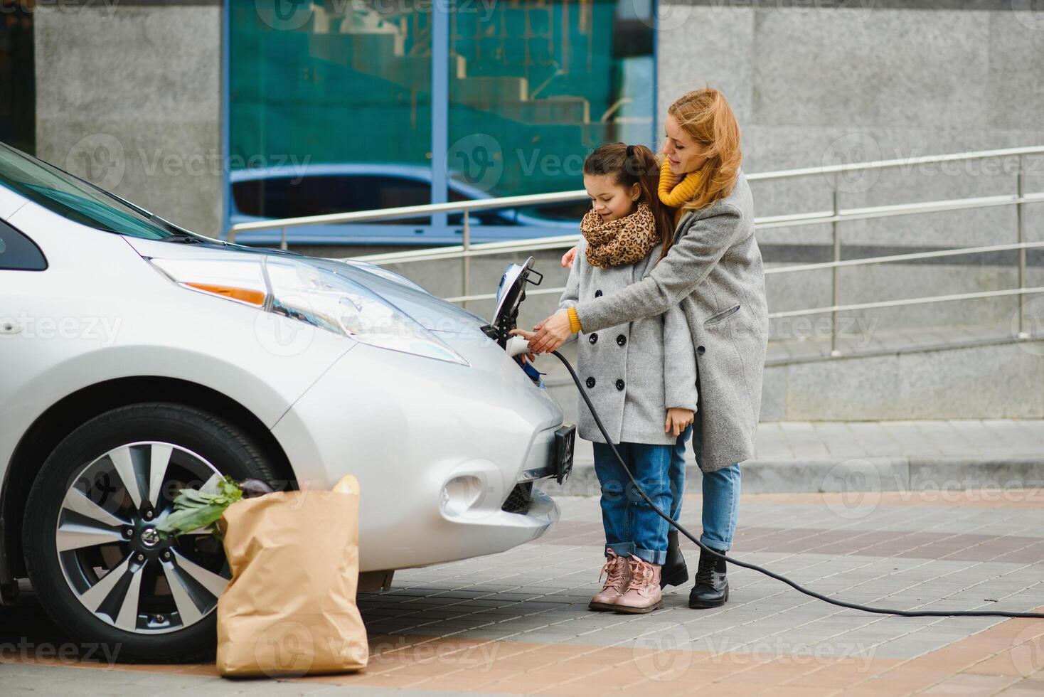 uma à moda mãe ensina dela filha quão para devidamente carregar a elétrico carro. foto