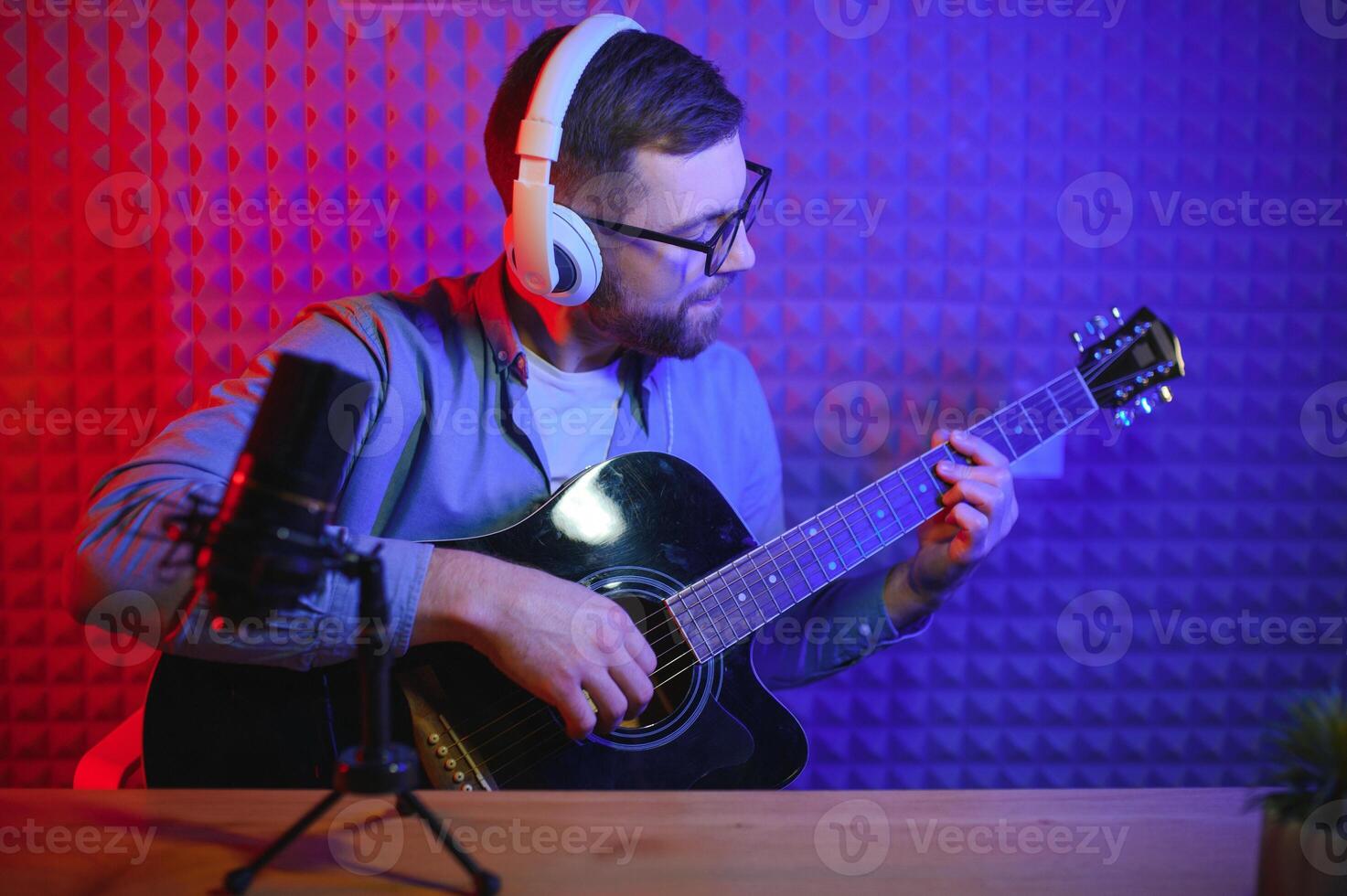 uma jovem à moda cara com uma barba vestindo casual ou música professor jogando guitarra dentro frente do Smartphone Câmera. conectados guitarra Treinamento ou vocal lição foto