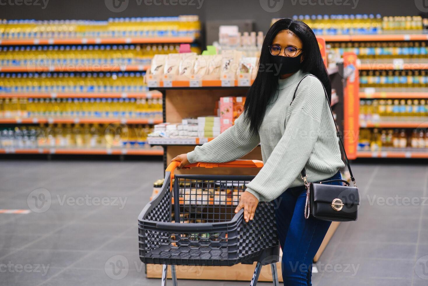 africano mulher vestindo descartável médico mascarar compras dentro supermercado durante coronavírus pandemia surto. epidemia Tempo foto