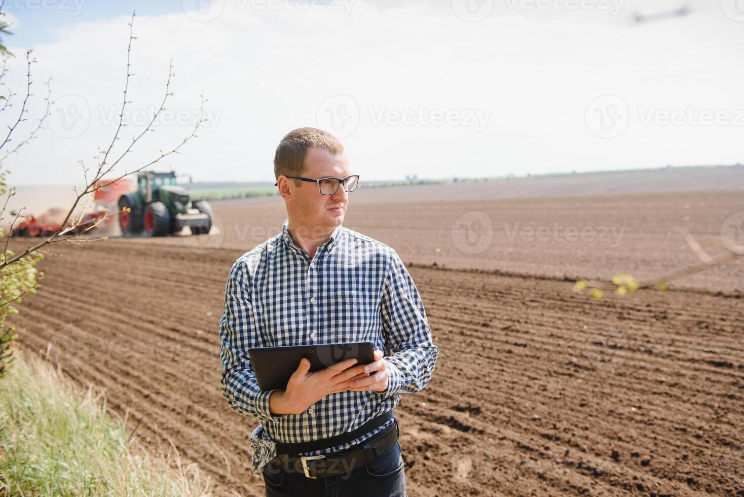 jovem agricultor em terras agrícolas com trator dentro fundo foto