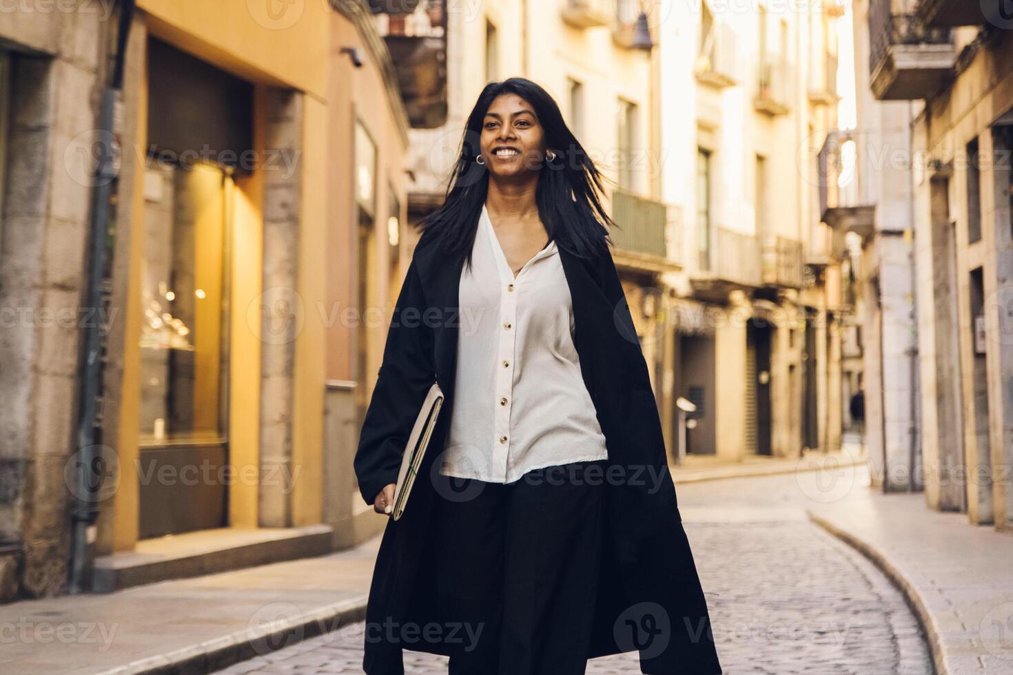 jovem mulher caminhando através a cidade usando uma dispositivo foto