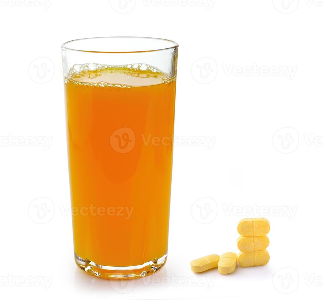 copo cheio de suco de laranja e pílulas de vitamina c isoladas no fundo branco foto