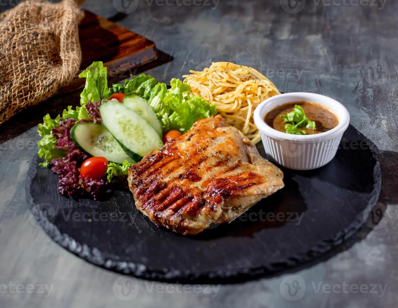 grelhado desossado frango bife com Pimenta molho, salada, Macarrão dentro uma prato lado Visão em Sombrio fundo foto