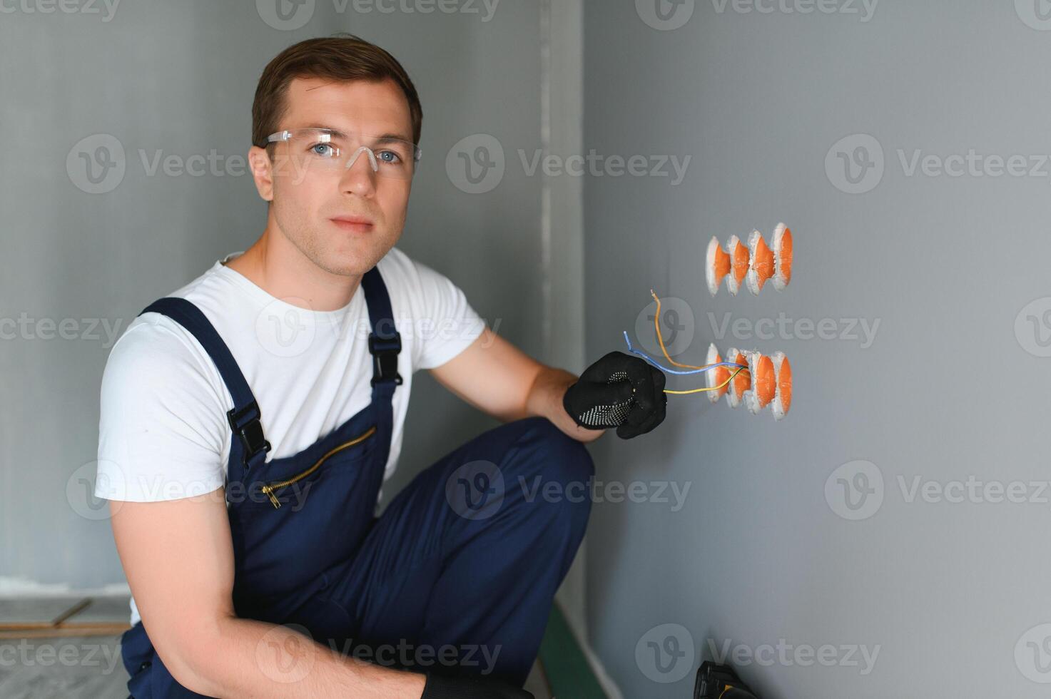 eletricista dentro uniforme montagem elétrico tomadas em a branco parede dentro de casa foto