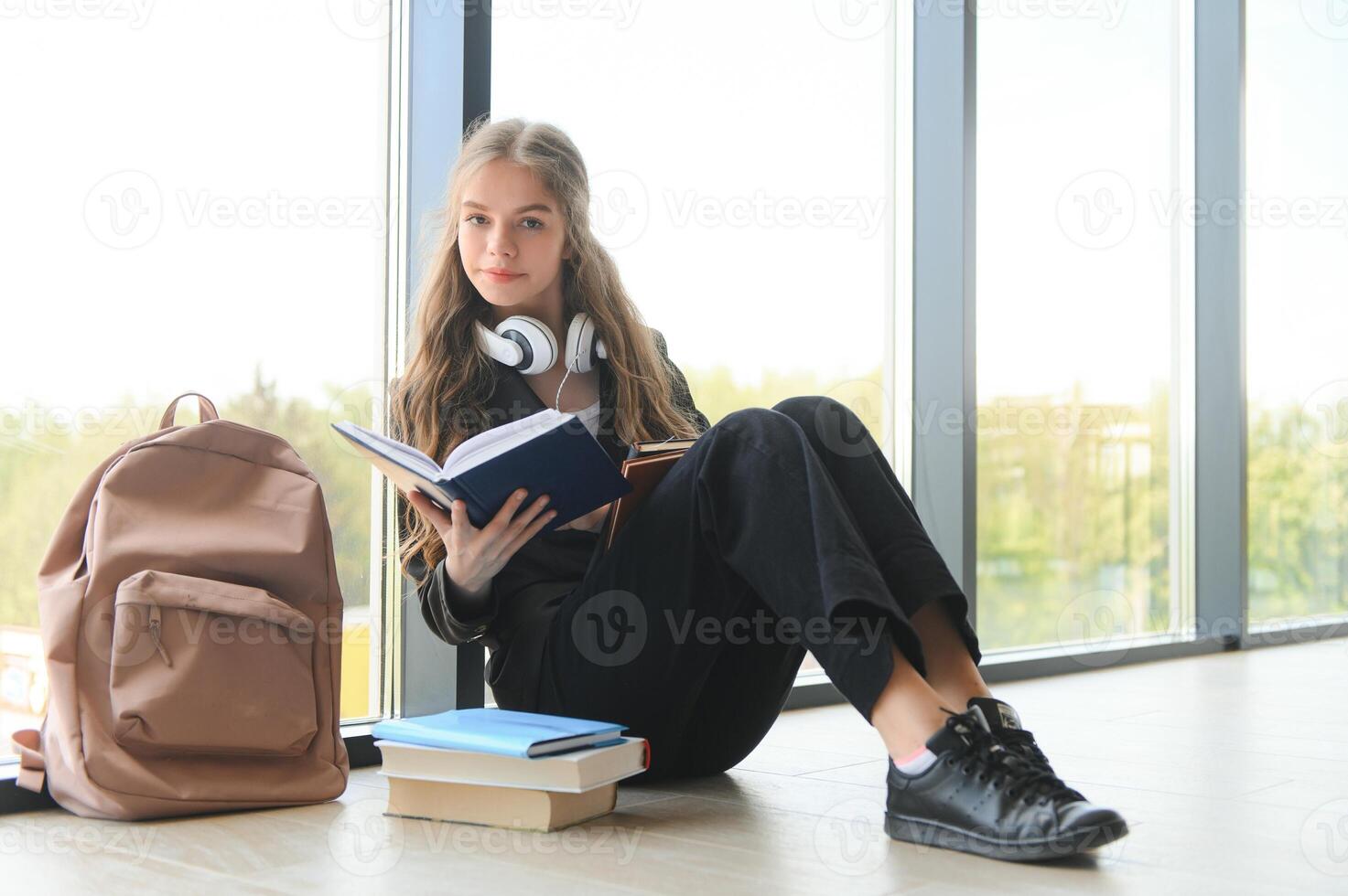 menina sorridente. lindo estudante sorridente enquanto sentado perto janela e lendo livro foto