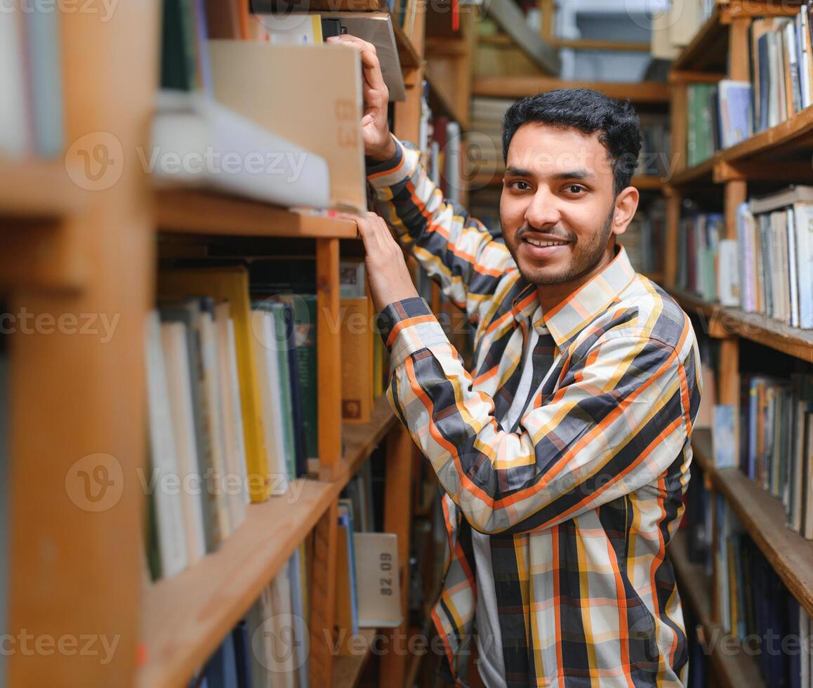 feliz inteligente indiano ou árabe cara, misturado raça macho, universidade estudante, dentro a biblioteca foto