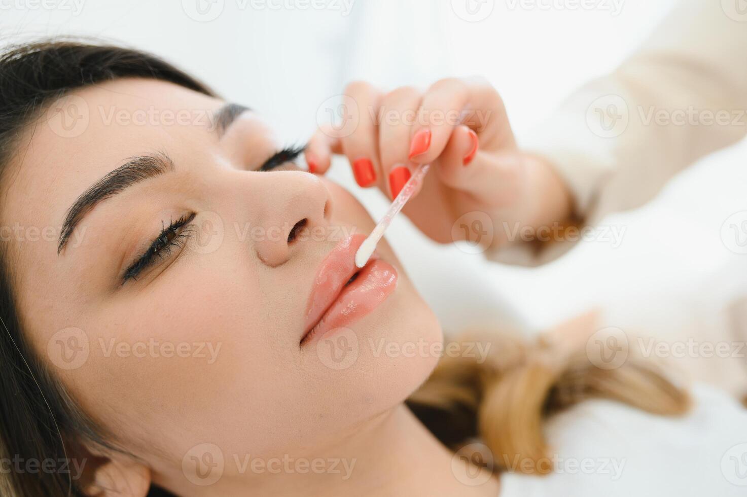 saudável spa jovem lindo mulher tendo permanente Maquiagem em dela lábios. fechar-se foto
