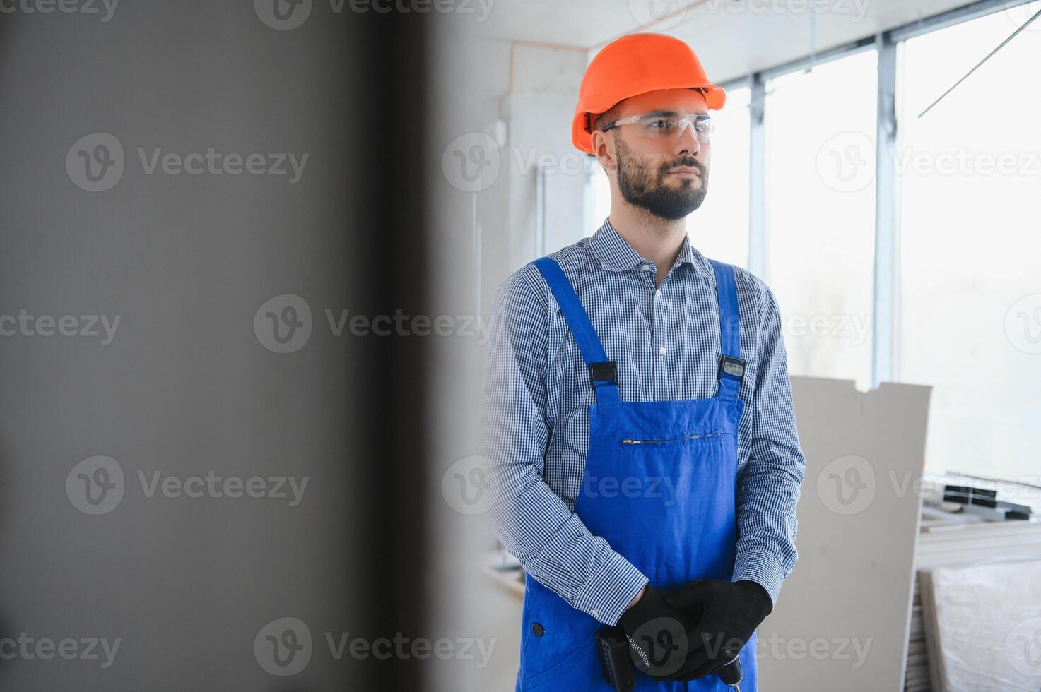 retrato do jovem e trabalha duro construtor posando dentro grande inacabado sala. construção conceito foto