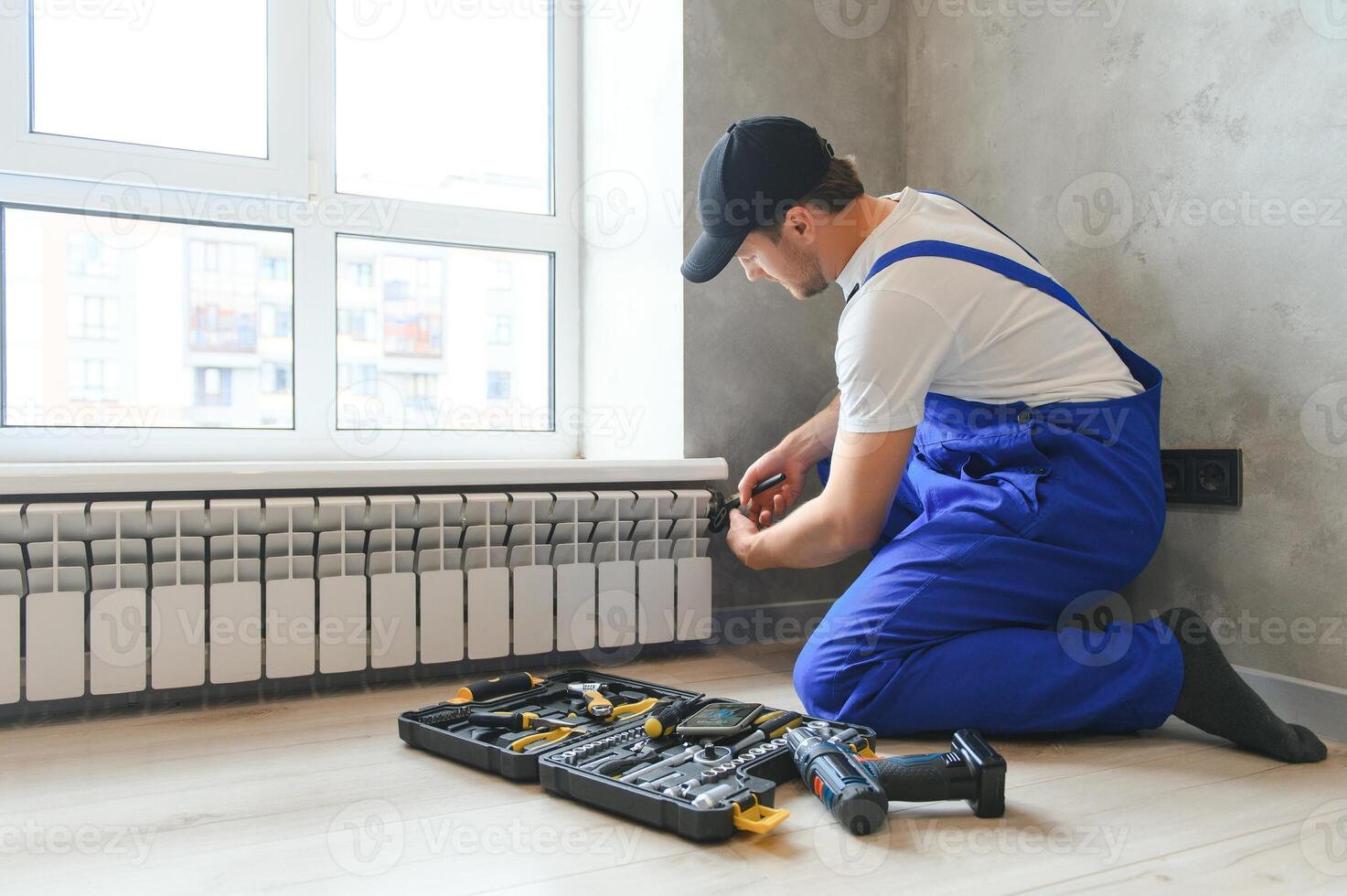 jovem homem encanador verificação radiador enquanto instalando aquecimento sistema dentro apartamento foto