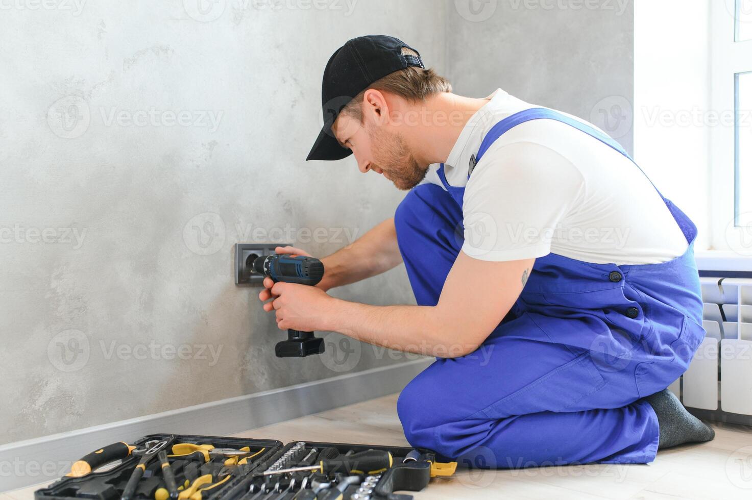 sorridente profissional eletricista dentro uniforme substituindo uma tomada dentro apartamento depois de renovação trabalhos foto