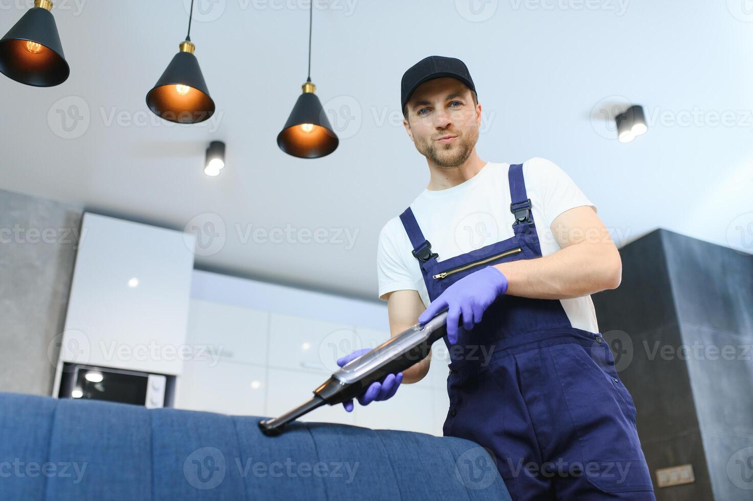 limpeza serviço. homem zelador dentro luvas e uniforme vácuo limpar \ limpo sofá com profissional equipamento. foto