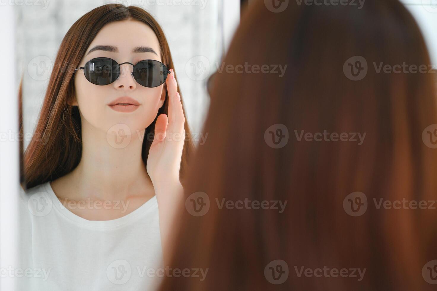 ela fez dela escolha. lindo jovem mulher ajustando dela Novo oculos de sol e sorridente enquanto em pé dentro ótico loja. foto