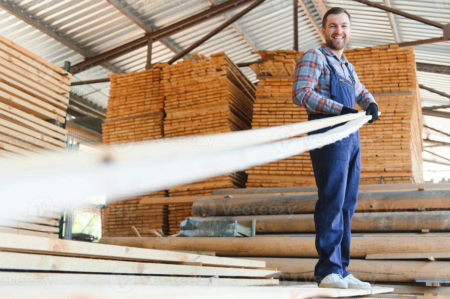 retrato do uma bonito trabalhador escolhendo a melhor de madeira Pranchas. carpinteiro em pé Próximo para uma grande pilha do madeira bares dentro uma armazém. foto