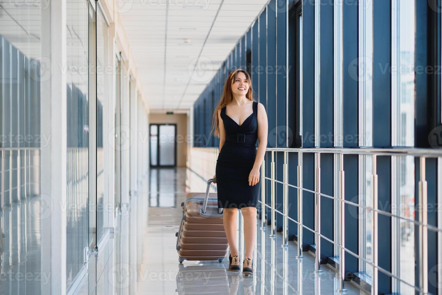 à moda mulher dentro uma Preto vestir com uma mala de viagem dentro a aeroporto terminal esperando para uma avião. foto