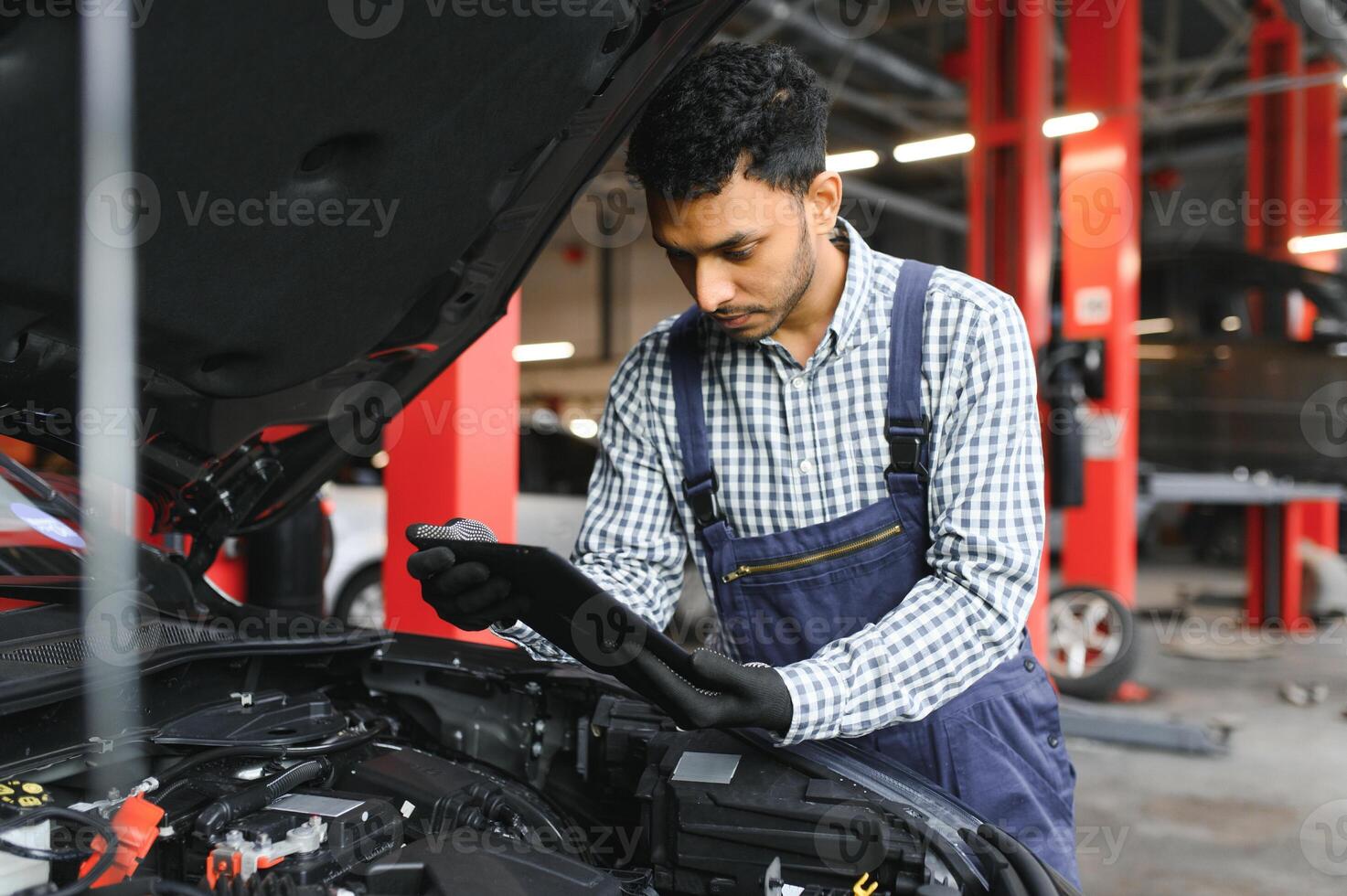 indiano carro mecânico em pé e trabalhando dentro serviço estação. carro especialistas examinando a levantado carro. profissional reparadores vestindo mecânico uniforme dentro azul cor. foto