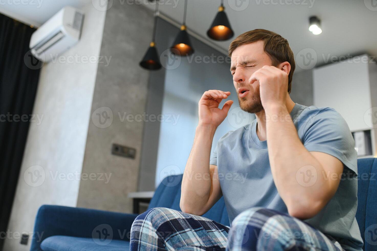 sentindo estressado. jovem bonito frustrado tocando sua cabeça e mantendo os olhos fechados enquanto está sentado no sofá em casa foto