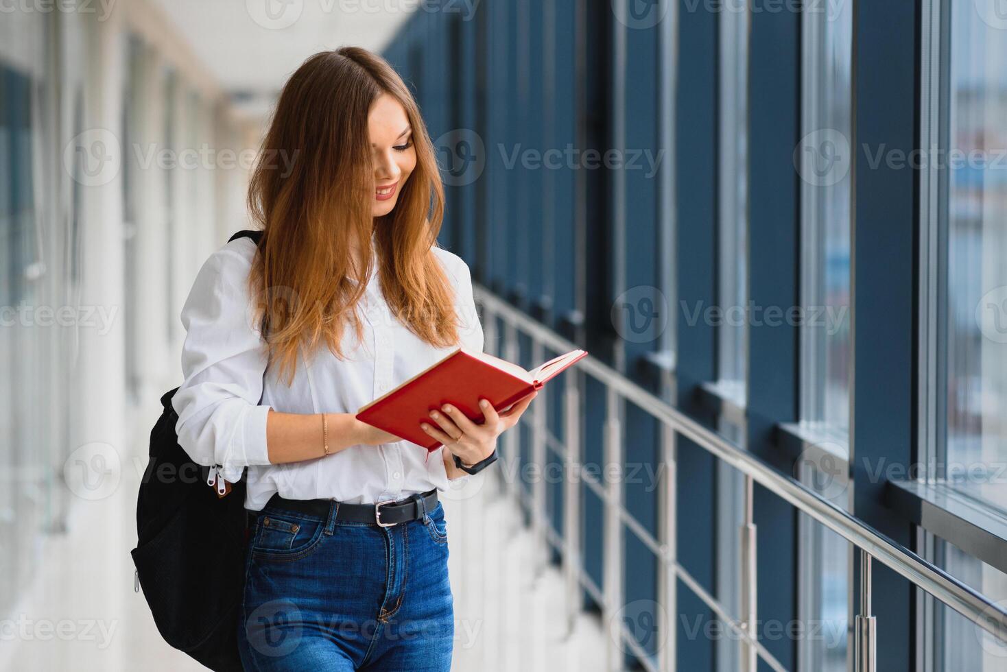 positividade lindo menina sorridente às Câmera, em pé em corredor com notas Como mochila, indo para lição. feliz morena fêmea aluna estudando dentro luxo universidade. foto