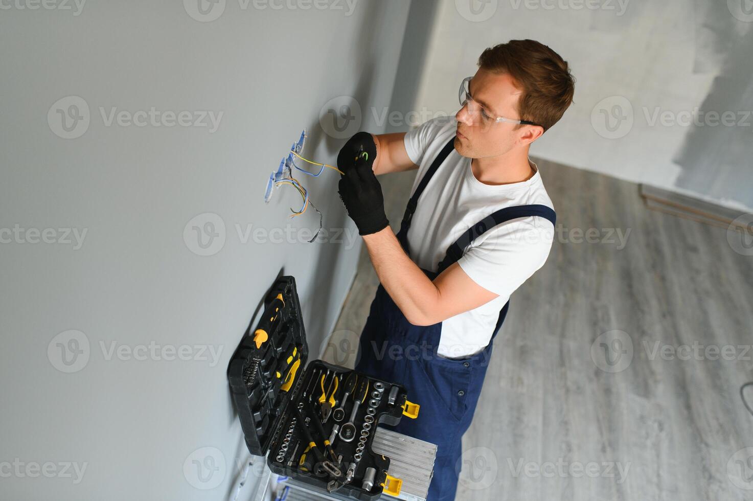 eletricista dentro uniforme montagem elétrico tomadas em a branco parede dentro de casa foto