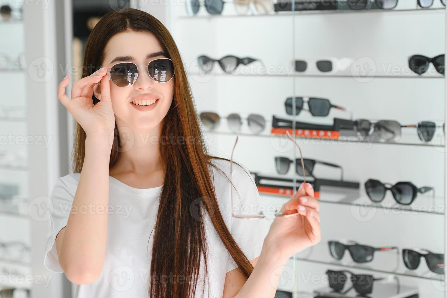 ela fez dela escolha. lindo jovem mulher ajustando dela Novo oculos de sol e sorridente enquanto em pé dentro ótico loja. foto